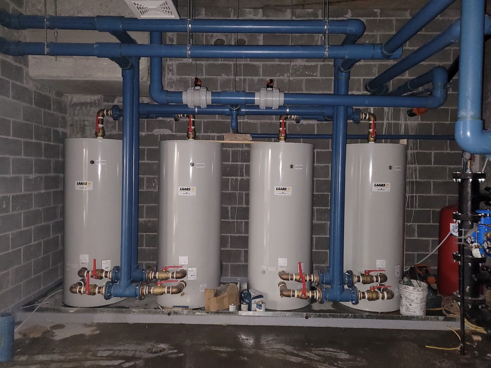 Four hot water tanks installed side by side with blue steel pipework in a mechanical room